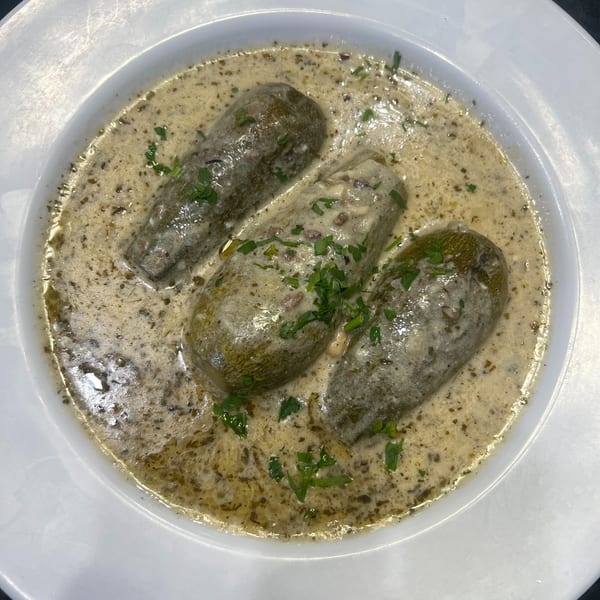 Three stuffed zucchini in a creamy sauce, garnished with fresh parsley, served in a white bowl.