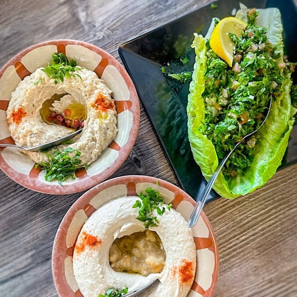 Two bowls of Omaya's Lebanese baba ghanoush and a plate of tabbouleh salad with a lemon wedge.