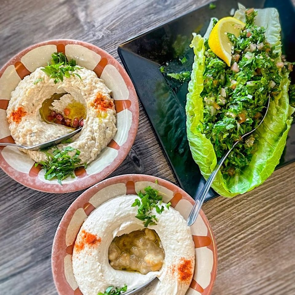 Two bowls of Omaya's Lebanese baba ghanoush and a plate of tabbouleh salad with a lemon wedge.