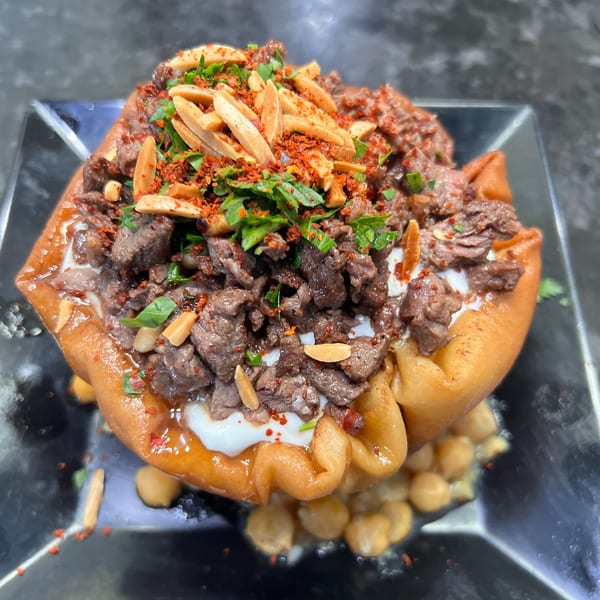Lebanese Fatteh with beef, yogurt, chickpeas, fried pita, parsley, and almonds on a dark plate.