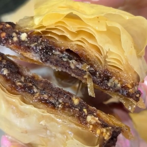 Close-up of a cut baklava pastry, revealing layers of phyllo dough and a dark, nutty filling.