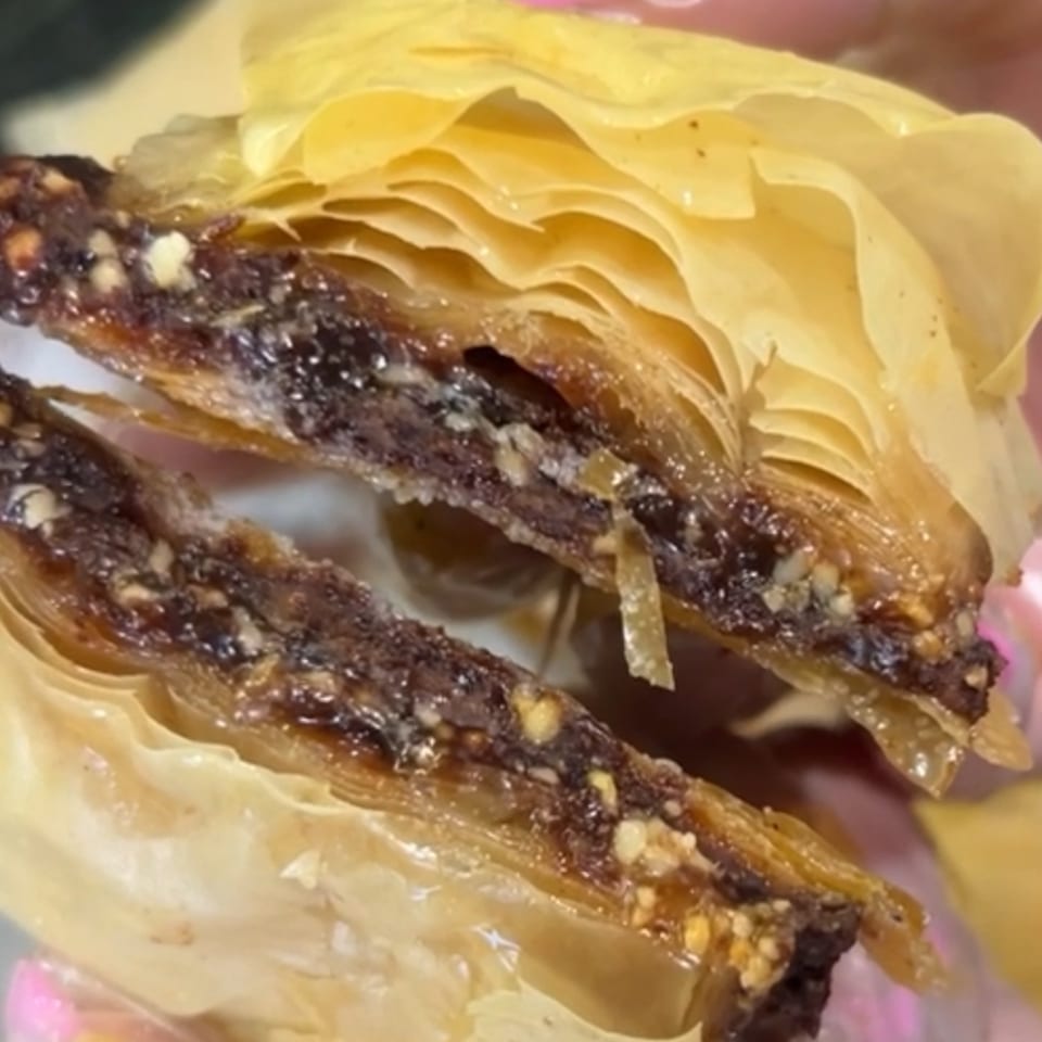 Close-up of a cut baklava pastry, revealing layers of phyllo dough and a dark, nutty filling.