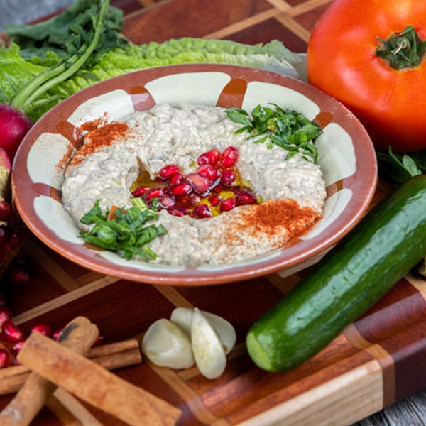 Omaya’s Lebanese Cuisine baba ghanoush topped with pomegranate seeds, parsley, and paprika, surrounded by fresh vegetables.