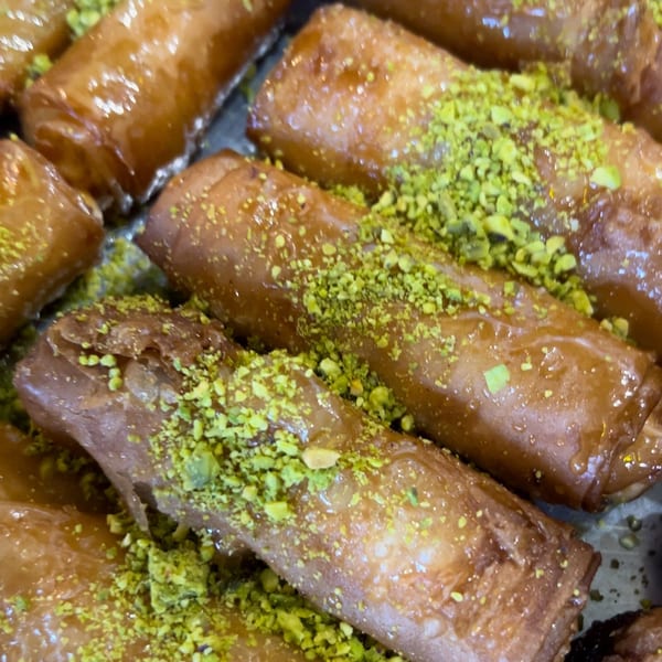 Close-up of golden Lebanese baklava rolls, glistening with syrup and sprinkled with green pistachios.