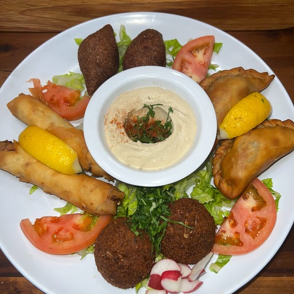 A white plate with a variety of Lebanese appetizers, including kibbeh, falafel, and hummus.