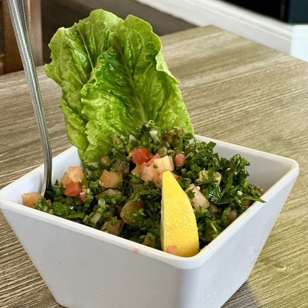 Omaya’s Lebanese Cuisine's tabbouleh salad with a lemon wedge and lettuce in a white bowl.