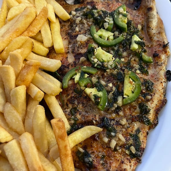 Grilled fish with green peppers and herbs, served with a side of golden french fries.