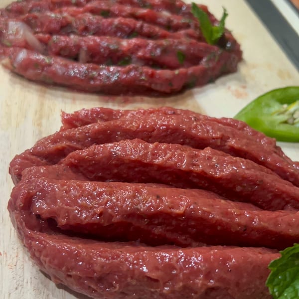 Two servings of raw kibbeh, a Lebanese dish, garnished with fresh mint leaves on a wooden board.