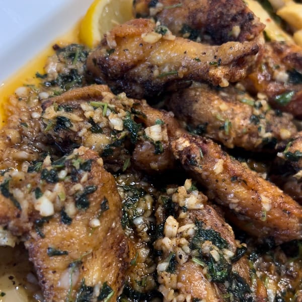 Close-up of Omaya's Lebanese Cuisine garlic chicken wings, glistening with sauce, herbs, and lemon.